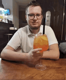 a man sitting at a table with a glass of orange liquid in front of a budweiser sign