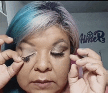 a woman with blue hair is applying makeup in front of a sign that says " aimer "