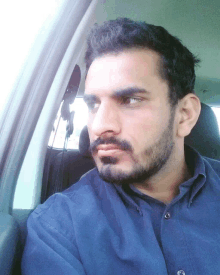 a man with a beard wearing a blue shirt is sitting in a car and looking out the window