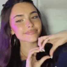 a woman is making a heart shape with her hands and smiling .