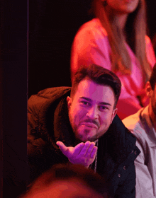 a man in a black jacket is sitting in a dark room with a woman in a pink shirt behind him