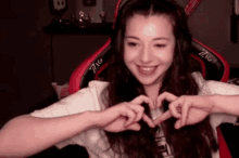 a woman wearing headphones is making a heart shape with her hands while sitting in a gaming chair .