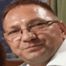 a close up of a man wearing glasses and a white shirt smiling .