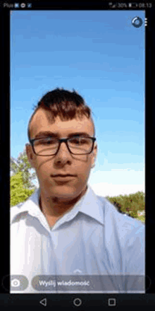 a man wearing glasses and a white shirt is taking a selfie on his phone .