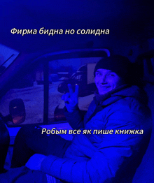 a man in a blue jacket is giving a peace sign while sitting in a car