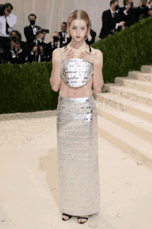 a woman wearing a silver top and a silver skirt stands on a staircase