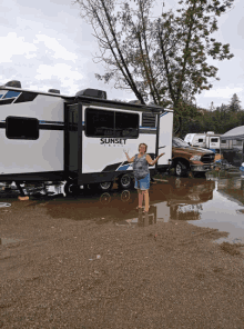 a woman stands in a puddle in front of a sunset trail trailer