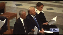 a man in a suit and tie is sitting next to a woman holding a piece of paper and a sign that says c-span