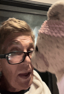 a man wearing glasses kisses a stuffed animal on the cheek