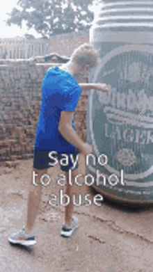 a man in a blue shirt is standing in front of a giant beer can that says " say no to alcohol abuse "