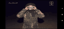 a man in a camouflage jacket looks through binoculars with the number 3 on the bottom