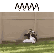 a man is sitting on the ground in front of a fence with the words aaaa written above him .