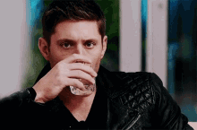 a man in a leather jacket drinking from a glass