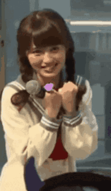 a girl in a school uniform is smiling and holding a microphone in her hand .