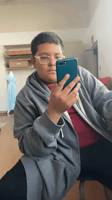 a boy wearing glasses is taking a picture of himself with his cell phone