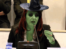 a woman in a witch costume is speaking into a microphone next to a glass of cristal water