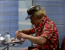 a man wearing a hat and a red shirt is sitting at a table with a tray of food .