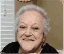 a woman with gray hair is smiling for the camera while sitting in front of a window .