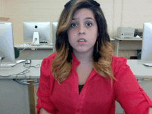 a woman in a red shirt is sitting at a desk in front of an apple computer