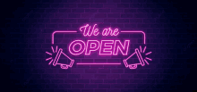 a neon sign that says we are open on a dark brick wall