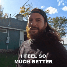 a man with a beard is standing in front of a house and says " i feel so much better "