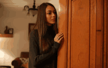 a woman in a black sweater is peeking out from behind a door