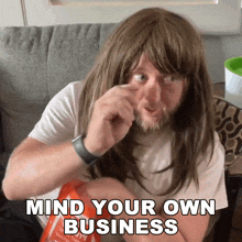 a man with long hair and a beard is eating a bag of chips with the words mind your own business above him