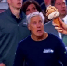 a man in a seahawks shirt is holding an ice cream cone while watching a game .