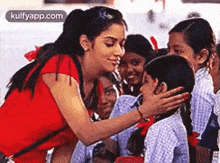 a woman in a red shirt is touching the face of a little girl in a crowd of children .