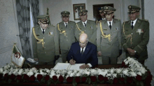 a group of men in military uniforms are standing around a man signing a book