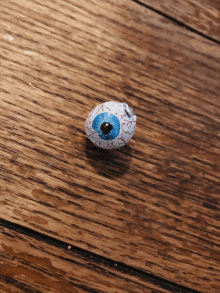 a fake eye with a blue pupil is on a wooden surface