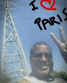 a man giving a peace sign in front of a power tower with the words i love paris written on it