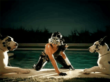 a woman in a mask is kneeling on the edge of a pool with two dalmatian dogs