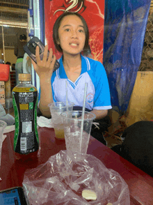 a girl sits at a table with a bottle of tea long leaf plus in front of her