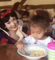 a little girl is sitting at a table with a plate of food and a woman dressed as snow white .