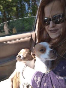 a woman wearing sunglasses holds two small dogs in her lap