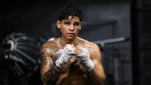 a shirtless boxer is wrapping his hands in boxing gloves in a dark room .