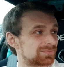 a man with a red beard is sitting in a car with a seat belt on .