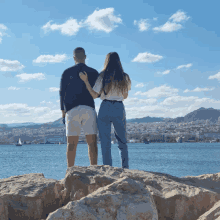 a man and a woman standing on rocks overlooking the ocean