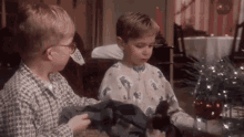 two young boys are standing next to each other in front of a christmas tree in a living room .