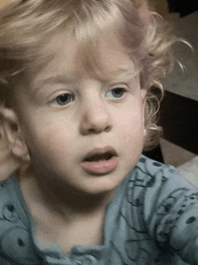 a little girl with blonde hair and blue eyes is wearing a blue shirt