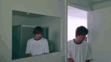 a man in a white shirt is looking at his reflection in the mirror