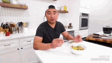 a man in a black shirt is sitting at a table with a bowl of food in front of him with the words made in animatica visible