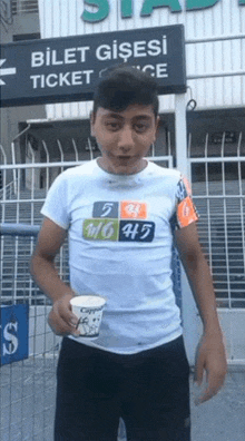 a young boy is holding a cup of coffee in front of a sign that says bilet gisesi ticket office .