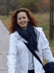 a woman wearing a white jacket and a blue scarf smiles while walking down a road .