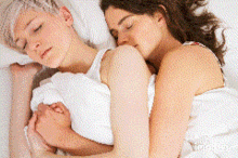 two women are hugging each other while laying in bed