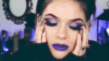 a woman with purple eyeshadow and purple lipstick is covering her face with her hands