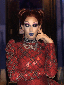 a drag queen wearing a red plaid dress and a choker with a necklace that says ' a ' on it