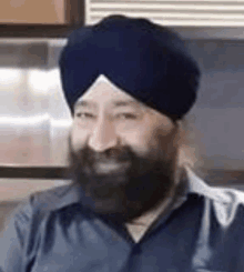 a man with a beard wearing a turban and a blue shirt is smiling .