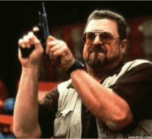 a man with a beard and sunglasses holds a gun in his right hand